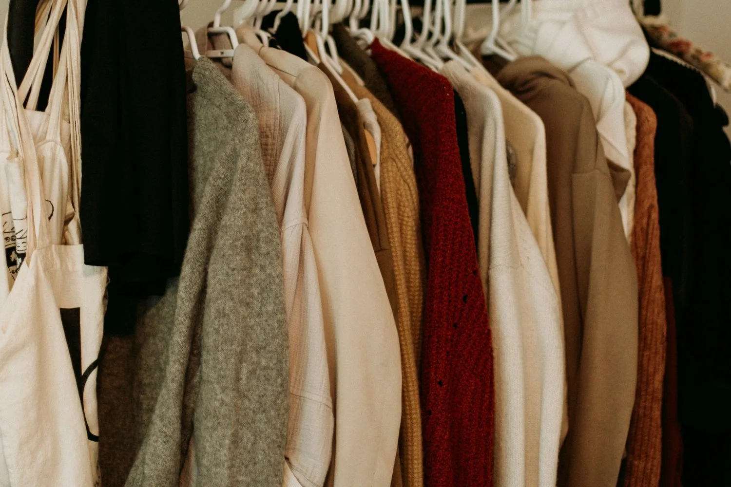Clothing rack with sweaters and knitwear in neutral tones including cream, gray, burgundy and brown
