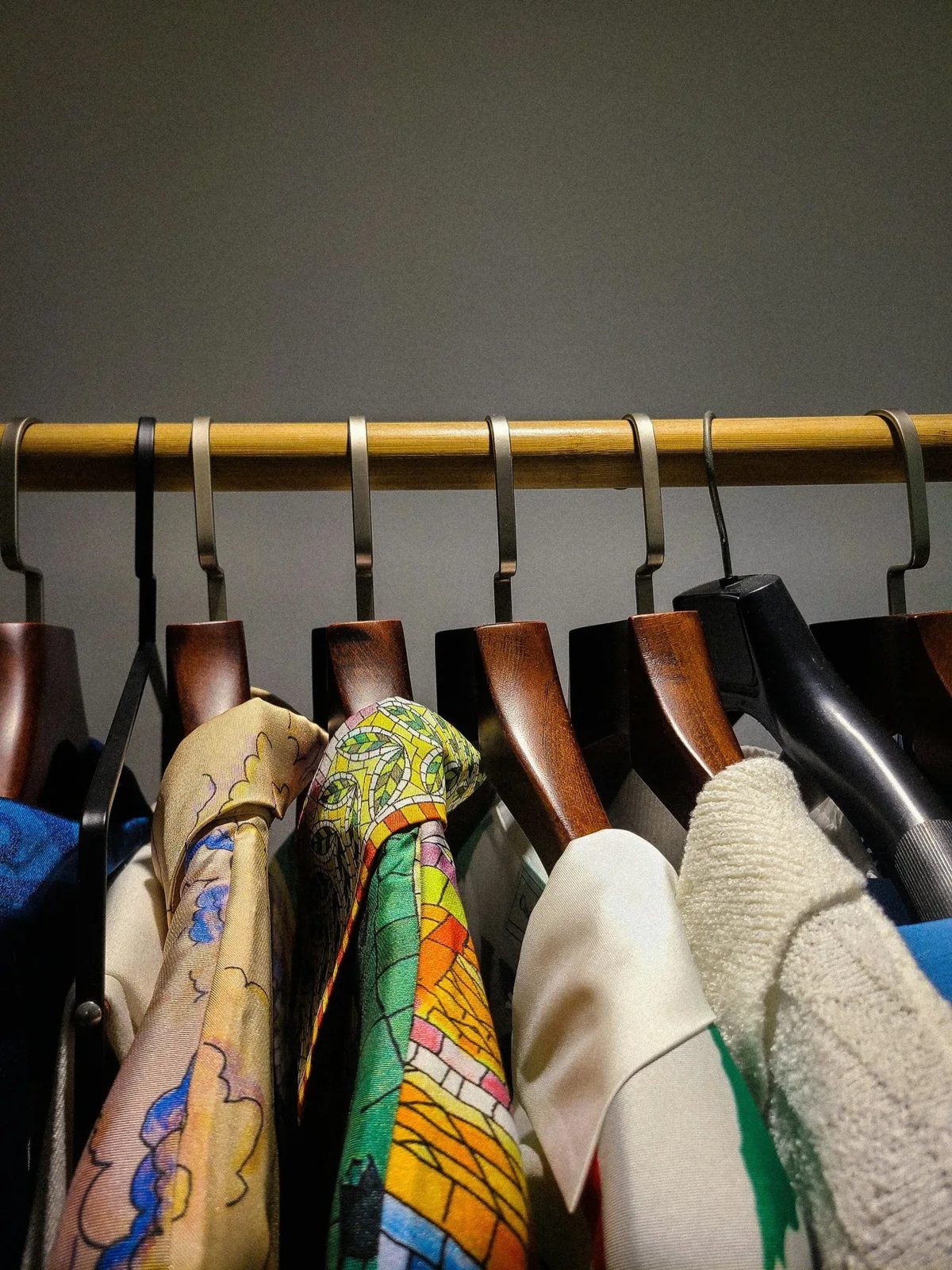 Colorful scarves and garments hanging on wooden hangers with metal hooks on a bamboo rod