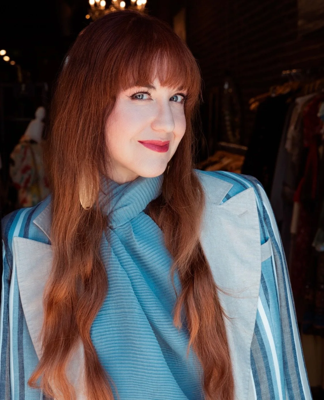 Woman with long reddish-brown hair and bangs wearing a blue striped blazer at an event
