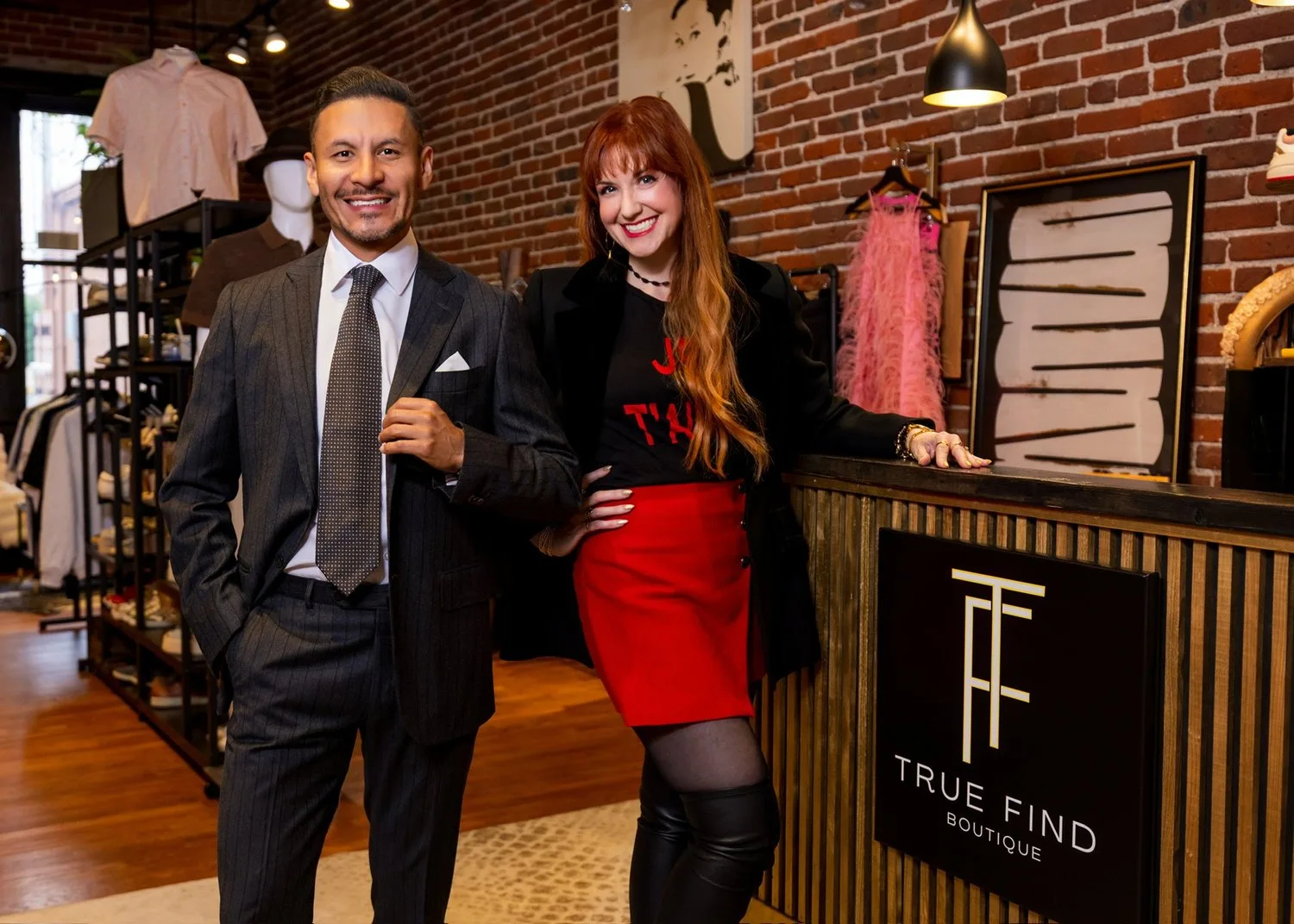 Two people smiling at True Find Boutique counter with brick walls and clothing displays