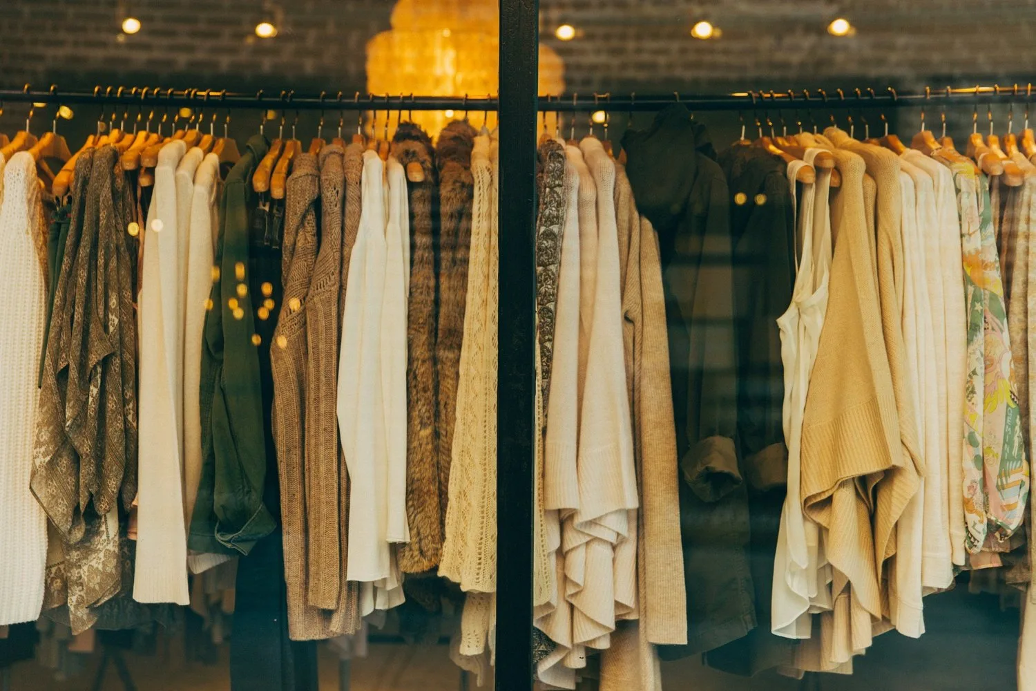 Neutral-toned clothing hanging on black rods in a retail store window with warm lighting